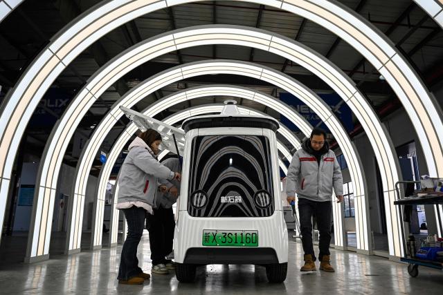 This photo taken on December 4, 2025 shows employees checking a newly manufactured Neolix X3 vehicle at a factory of Chinese autonomous delivery vehicle maker Neolix in Yancheng, in eastern China's Jiangsu province. In a light-filled workshop in eastern China, a robotic arm moved a partially assembled autonomous vehicle as workers calibrated its cameras, typical of the incremental automation being adopted even across smaller factories in the world's manufacturing powerhouse. (Photo by Jade GAO / AFP) / To go with 'CHINA-ECONOMY-MANUFACTURING-TECHNOLOGY-AI, FOCUS' by Jing Xuan TENG