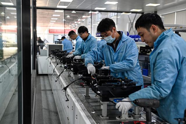 This photo taken on December 4, 2025 shows employees working on a Neolix X3 vehicle production line at a factory of Chinese autonomous delivery vehicle maker Neolix in Yancheng, in eastern China's Jiangsu province. In a light-filled workshop in eastern China, a robotic arm moved a partially assembled autonomous vehicle as workers calibrated its cameras, typical of the incremental automation being adopted even across smaller factories in the world's manufacturing powerhouse. (Photo by Jade GAO / AFP) / To go with 'CHINA-ECONOMY-MANUFACTURING-TECHNOLOGY-AI, FOCUS' by Jing Xuan TENG