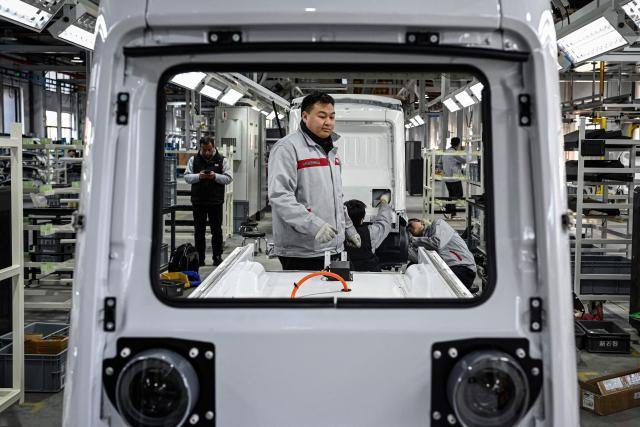 This photo taken on December 4, 2025 shows employees working on a Neolix X3 vehicle production line at a factory of Chinese autonomous delivery vehicle maker Neolix in Yancheng, in eastern China's Jiangsu province. In a light-filled workshop in eastern China, a robotic arm moved a partially assembled autonomous vehicle as workers calibrated its cameras, typical of the incremental automation being adopted even across smaller factories in the world's manufacturing powerhouse. (Photo by Jade GAO / AFP) / To go with 'CHINA-ECONOMY-MANUFACTURING-TECHNOLOGY-AI, FOCUS' by Jing Xuan TENG
