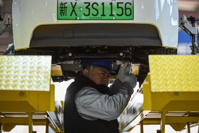 This photo taken on December 4, 2025 shows an employee working on a Neolix X3 vehicle production line at a factory of Chinese autonomous delivery vehicle maker Neolix in Yancheng, in eastern China's Jiangsu province. In a light-filled workshop in eastern China, a robotic arm moved a partially assembled autonomous vehicle as workers calibrated its cameras, typical of the incremental automation being adopted even across smaller factories in the world's manufacturing powerhouse. (Photo by Jade GAO / AFP) / To go with 'CHINA-ECONOMY-MANUFACTURING-TECHNOLOGY-AI, FOCUS' by Jing Xuan TENG