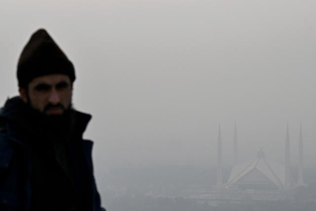 This picture taken on December 9, 2025, shows the Shah Faisal Mosque engulfed in dense smog due to severe air pollution in Islamabad. Checkpoints set up this month are part of a crackdown by authorities to combat the city's soaring smog levels, with winter months the worst due to atmospheric inversions that trap pollutants at ground level. While not yet at the extreme winter levels of Lahore or the megacity Karachi, where heavy industry and brick kilns spew tons of pollutants each year, Islamabad is steadily closing the gap. (Photo by Aamir QURESHI / AFP)