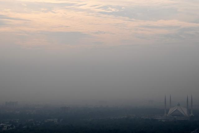 This picture taken on December 9, 2025, shows the Shah Faisal Mosque engulfed in dense smog due to severe air pollution in Islamabad. Checkpoints set up this month are part of a crackdown by authorities to combat the city's soaring smog levels, with winter months the worst due to atmospheric inversions that trap pollutants at ground level. While not yet at the extreme winter levels of Lahore or the megacity Karachi, where heavy industry and brick kilns spew tons of pollutants each year, Islamabad is steadily closing the gap. (Photo by Aamir QURESHI / AFP)