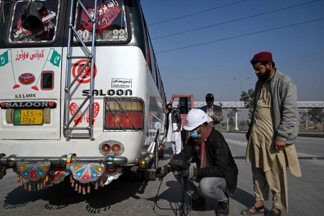 This picture taken on December 10, 2025, shows technician Waleed Ahmed (3R) examining a vehicle to test its emissions on road, on the outskirts of Islamabad. Checkpoints set up this month are part of a crackdown by authorities to combat the city's soaring smog levels, with winter months the worst due to atmospheric inversions that trap pollutants at ground level. While not yet at the extreme winter levels of Lahore or the megacity Karachi, where heavy industry and brick kilns spew tons of pollutants each year, Islamabad is steadily closing the gap. (Photo by Aamir QURESHI / AFP)