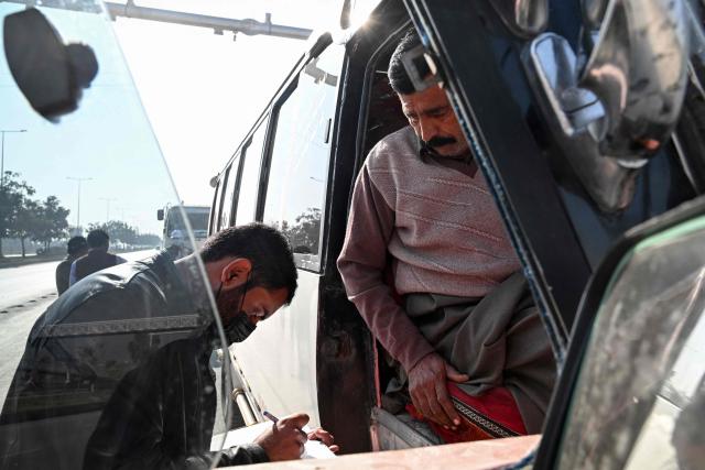 This picture taken on December 10, 2025, shows a technician (L) examining a vehicle to test its emissions on road, on the outskirts of Islamabad. Checkpoints set up this month are part of a crackdown by authorities to combat the city's soaring smog levels, with winter months the worst due to atmospheric inversions that trap pollutants at ground level. While not yet at the extreme winter levels of Lahore or the megacity Karachi, where heavy industry and brick kilns spew tons of pollutants each year, Islamabad is steadily closing the gap. (Photo by Aamir QURESHI / AFP)