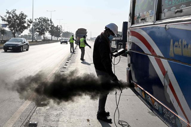 This picture taken on December 10, 2025, shows technician Waleed Ahmed (R) examining a vehicle to test its emissions on road, on the outskirts of Islamabad. Checkpoints set up this month are part of a crackdown by authorities to combat the city's soaring smog levels, with winter months the worst due to atmospheric inversions that trap pollutants at ground level. While not yet at the extreme winter levels of Lahore or the megacity Karachi, where heavy industry and brick kilns spew tons of pollutants each year, Islamabad is steadily closing the gap. (Photo by Aamir QURESHI / AFP)