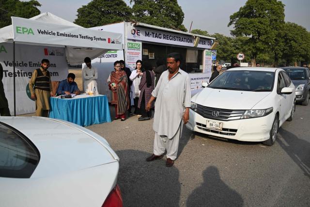 This picture taken on December 10, 2025, shows residents examining their cars at an emission testing point in Islamabad. Checkpoints set up this month are part of a crackdown by authorities to combat the city's soaring smog levels, with winter months the worst due to atmospheric inversions that trap pollutants at ground level. While not yet at the extreme winter levels of Lahore or the megacity Karachi, where heavy industry and brick kilns spew tons of pollutants each year, Islamabad is steadily closing the gap. (Photo by Aamir QURESHI / AFP)