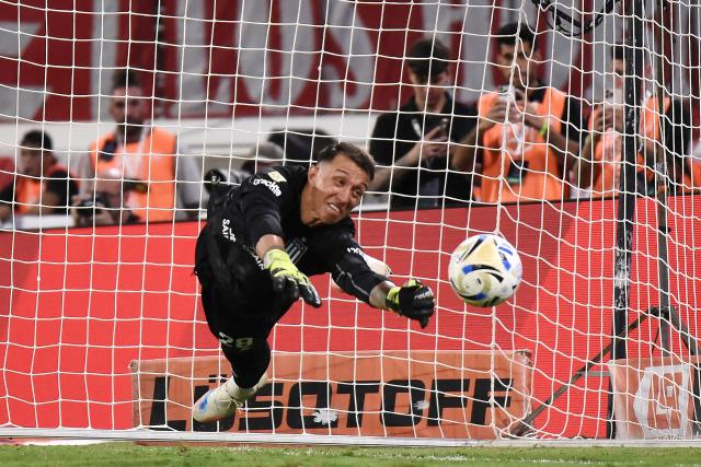 TOPSHOT - Estudiantes' Uruguayan goalkeeper #28 Fernando Muslera makes a save past Racing's Uruguayan defender #15 Gaston Martirena (out of frame) during the penalty shootout of the Argentine Professional Football League 2025 Clausura Tournament final match between Racing and Estudiantes at the Madre de Ciudades stadium in Santiago del Estero, Argentina on December 13, 2025. (Photo by Luis Santillan / AFP)