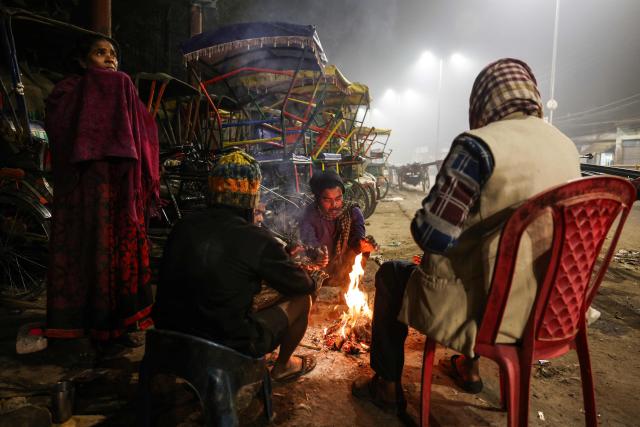 People surround a bonfire along a roadside on a cold winter morning in Varanasi on December 14, 2025. (Photo by Niharika KULKARNI / AFP)