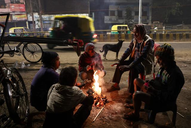 People surround a bonfire along a roadside on a cold winter morning in Varanasi on December 14, 2025. (Photo by Niharika KULKARNI / AFP)