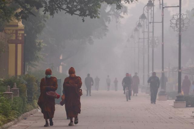 Monks wearing anti-pollution masks walk along a street on a smoggy morning in Sarnath on the outskirts of Varanasi on December 14, 2025. (Photo by Niharika KULKARNI / AFP)