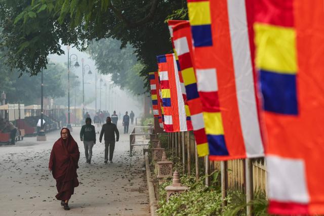 A monk walks past Buddhist flags along a street on a smoggy morning in Sarnath on the outskirts of Varanasi on December 14, 2025. (Photo by Niharika KULKARNI / AFP)