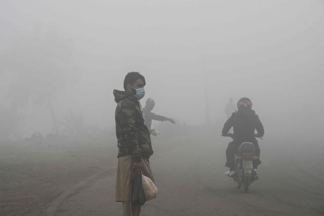 A man wearing an anti-pollution mask stands along a street amid dense smog in Lahore on December 14, 2025. (Photo by Arif ALI / AFP)