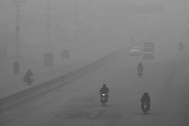 Commuters ride along a street amid dense smog in Lahore on December 14, 2025. (Photo by Arif ALI / AFP)