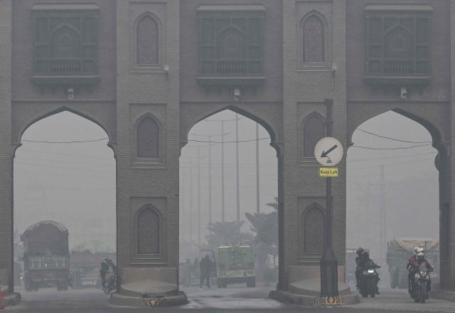 Commuters ride along a street amid dense smog in Lahore on December 14, 2025. (Photo by Arif ALI / AFP)