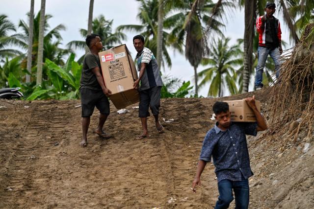 People carry medical supplies before crossing a river after a bridge was damaged by flooding in Juli, in Indonesia's Aceh province on December 14, 2025. Devastating floods and landslides have killed 1,006 people in Indonesia, rescuers said December 13 as the Southeast Asian nation grapples with the huge scale of relief efforts. (Photo by CHAIDEER MAHYUDDIN / AFP)