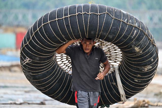 A man carries a tube for crossing a river after a bridge was damaged by flooding in Juli, in Indonesia's Aceh province on December 14, 2025. Devastating floods and landslides have killed 1,006 people in Indonesia, rescuers said December 13 as the Southeast Asian nation grapples with the huge scale of relief efforts. (Photo by CHAIDEER MAHYUDDIN / AFP)