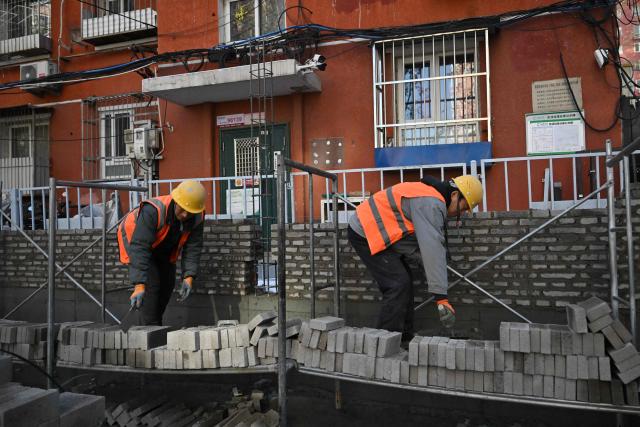 Workers build a wall of a residential building in Beijing on December 14, 2025. (Photo by Pedro PARDO / AFP)