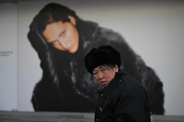 A woman walks past a shopping mall in Beijing on December 14, 2025. (Photo by Pedro PARDO / AFP)