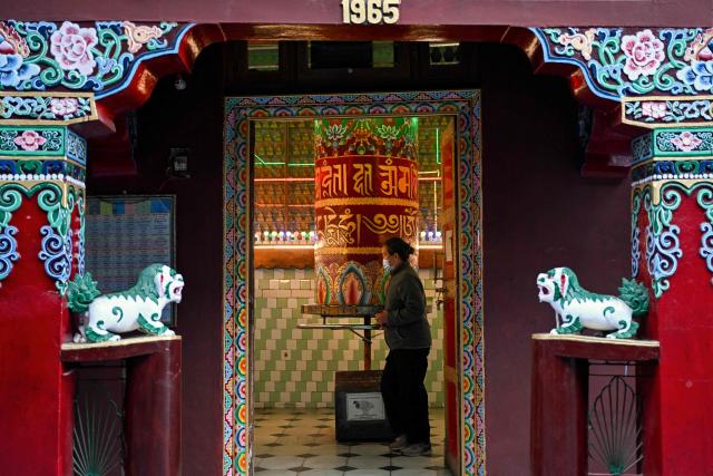 A woman wearing an anti-pollution mask offers prayers at a Tibetan Buddhist temple in McLeod Ganj near Dharamsala on December 14, 2025. (Photo by Arun SANKAR / AFP)