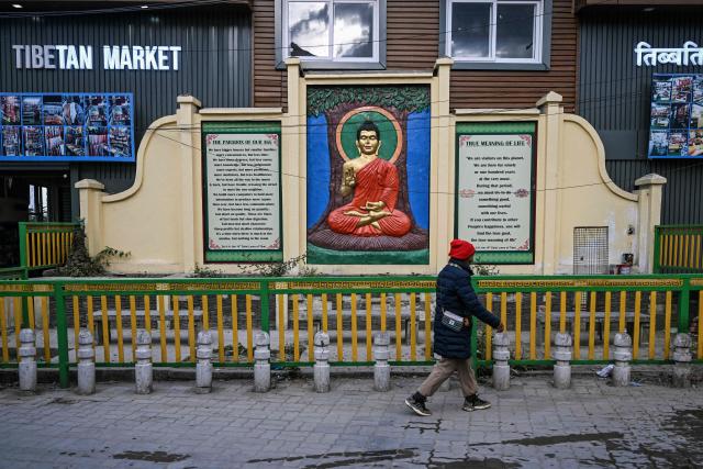 A woman walks past a relief wall mural of Buddha along a street in McLeod Ganj near Dharamsala on December 14, 2025. (Photo by Arun SANKAR / AFP)