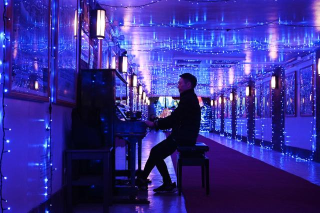 A man plays the piano at a winter festival lighting display at Ryogoku station in Tokyo on December 14, 2025. (Photo by GREG BAKER / AFP)