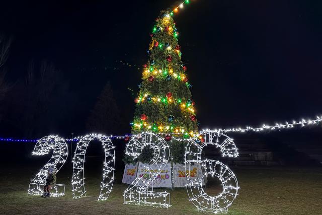 A child sits on an illuminated installation for the upcoming year 2026 next to a Christmas tree in Zaporizhzhia on December 13, 2025, amid the Russian invasion of Ukraine. (Photo by Darya NAZAROVA / AFP)