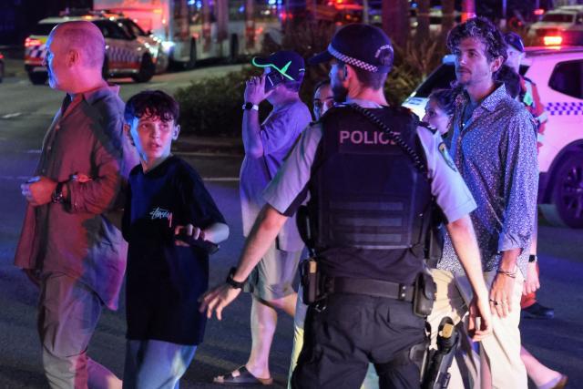 A policeman ushers people across a street after a shooting incident at Bondi Beach in Sydney on December 14, 2025. Australian police said two people were in custody following reports of multiple gunshots on December 14 at Sydney's famed Bondi Beach, urging the public to take shelter. (Photo by DAVID GRAY / AFP)