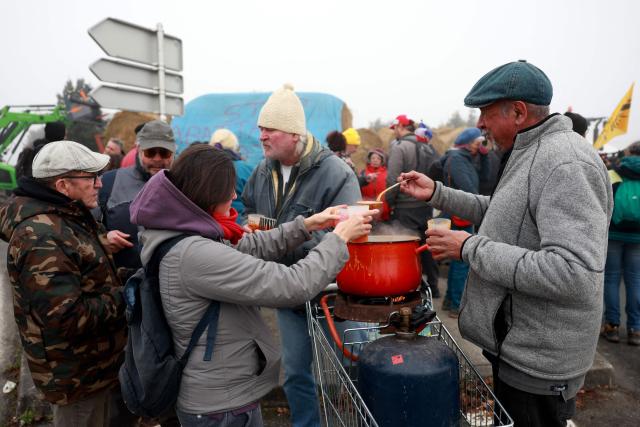 Farmers drink soup to warm themselves up while they filter access near the Rives d'Arcins shopping center in Bègles, on the outskirts of Bordeaux, south-western France, on December 14, 2025, to protest against the health policy put in place to eradicate lumpy skin disease affecting cattle. On December 12, 2025 French veterinarians slaughtered a herd of cows thought to be diseased after police dispersed angry farmers trying to protect them, an AFP reporter said, as an agricultural union called for nationwide protests. French farmers are unhappy with the state's management of an outbreak of nodular dermatitis -- widely known as lumpy skin disease. (Photo by ROMAIN PERROCHEAU / AFP)