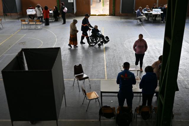 An elederly lady in a wheelchair arrives at a polling station during the presidential runoff election in Santiago on December 14, 2025. Chileans head to the polls for a presidential runoff between Jeannette Jara, a communist backed by a broad left coalition, and Jose Antonio Kast, a devout far-right politico promising a hard line on security and migration. (Photo by RODRIGO ARANGUA / AFP)