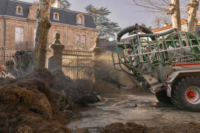 A tractor sprays liquid manure on the facade of Millau's sub-prefecture during a farmers' protest against the policy of slaughtering cows with Contagious Nodular Dermatosis (CND) in Millau, central France, on December 14, 2025. On December 12, 2025 French veterinarians slaughtered a herd of cows thought to be diseased after police dispersed angry farmers trying to protect them, an AFP reporter said, as an agricultural union called for nationwide protests. French farmers are unhappy with the state's management of an outbreak of nodular dermatitis -- widely known as lumpy skin disease. (Photo by Idriss Bigou-Gilles / AFP)