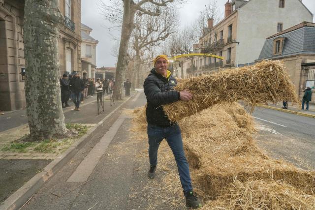 A member of French farmers unions Coordination Rurale stacks hay bails outside Millau's sub-prefecture during a farmers' protest against the policy of slaughtering cows with Contagious Nodular Dermatosis (CND) in Millau, central France, on December 14, 2025. On December 12, 2025 French veterinarians slaughtered a herd of cows thought to be diseased after police dispersed angry farmers trying to protect them, an AFP reporter said, as an agricultural union called for nationwide protests. French farmers are unhappy with the state's management of an outbreak of nodular dermatitis -- widely known as lumpy skin disease. (Photo by Idriss Bigou-Gilles / AFP)