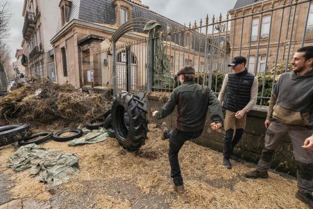 TOPSHOT - Farmers kick a tractor tyre towards a pile of debris outside of Millau's sub-prefecture during a farmers' protest against the policy of slaughtering cows with Contagious Nodular Dermatosis (CND) in Millau, central France, on December 14, 2025. On December 12, 2025 French veterinarians slaughtered a herd of cows thought to be diseased after police dispersed angry farmers trying to protect them, an AFP reporter said, as an agricultural union called for nationwide protests. French farmers are unhappy with the state's management of an outbreak of nodular dermatitis -- widely known as lumpy skin disease. (Photo by Idriss Bigou-Gilles / AFP)