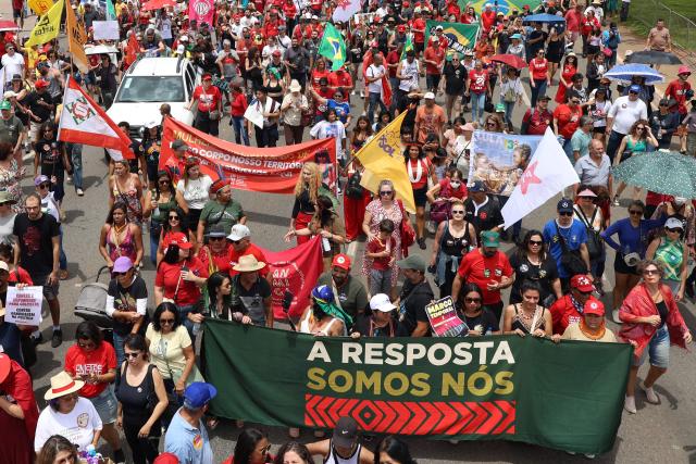 Demonstrators hold allusive signs during a protest against the Brazilian Congress to reject a bill that would modify penalties for crimes against democracy, hence reduce the sentence of former President Jair Bolsonaro, and the recent approval of a constitutional amendment incorporating the 'Marco Temporal' thesis, which attacks indigenous territoial rights, in Brasilia on December 14, 2025. (Photo by Sergio Lima / AFP)
