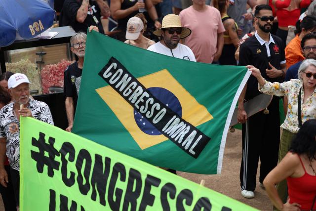 Demonstrators hold allusive signs during a protest against the Brazilian Congress to reject a bill that would modify penalties for crimes against democracy, hence reduce the sentence of former President Jair Bolsonaro, and the recent approval of a constitutional amendment incorporating the 'Marco Temporal' thesis, which attacks indigenous territoial rights, in Brasilia on December 14, 2025. (Photo by Sergio Lima / AFP)