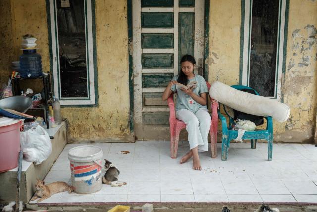 Rania, 16, a high school student, reads a book titled Bandung After Rain, which she saved during a flash flood, at her home in Aceh Tamiang, Northern Sumatra, on December 14, 2025. Devastating floods and landslides have killed 1,006 people in Indonesia, rescuers said on December 13 as the Southeast Asian nation grapples with the huge scale of relief efforts. (Photo by Yasuyoshi CHIBA / AFP)