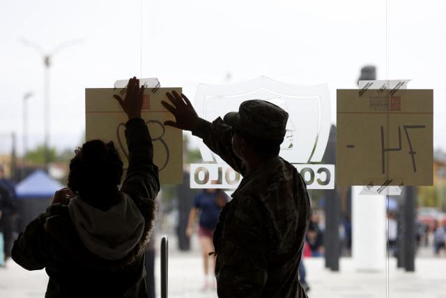 A soldier and a soman put up a poster during the presidential runoff election at Monumental Colo-Colo Stadium in Santiago, Chile on December 14, 2025. Chileans head to the polls for a presidential runoff between Jeannette Jara, a communist backed by a broad left coalition, and Jose Antonio Kast, a devout far-right politico promising a hard line on security and migration. (Photo by Raul BRAVO / AFP)