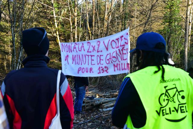 Protestors hold a banner reading "No to the two times two road, one minute won for 132 millions" as they take part in a march organised by "collectif Alouettes 147" against the project of a new road (2x2 between Couzeix and Nieul), in Nieul, central France on December 14, 2025. (Photo by PASCAL LACHENAUD / AFP)