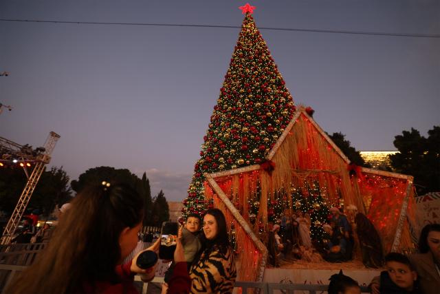 A woman holds her child as she poses for a photograph in front of a Christmas tree in Manger Square, in the Israeli-occupied West Bank city of Bethlehem on December 14, 2025. Christmas cheer returned to the traditional birthplace of Jesus Christ on December 6, 2025, the first time the city has held the usual celebrations since the outbreak of the war in Gaza following Hamas's attack on Israel in October 2023. (Photo by HAZEM BADER / AFP)