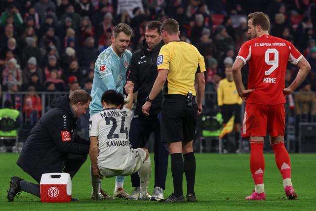 Bayern Munich's English forward #09 Harry Kane (R) looks on as Mainz' Japanese midfielder #24 Sota Kawasaki receives medical attention during the German first division Bundesliga football match between FC Bayern Munich and Mainz 05 in Munich, southern Germany on December 14, 2025. (Photo by Karl-Josef HILDENBRAND / AFP) / DFL REGULATIONS PROHIBIT ANY USE OF PHOTOGRAPHS AS IMAGE SEQUENCES AND/OR QUASI-VIDEO