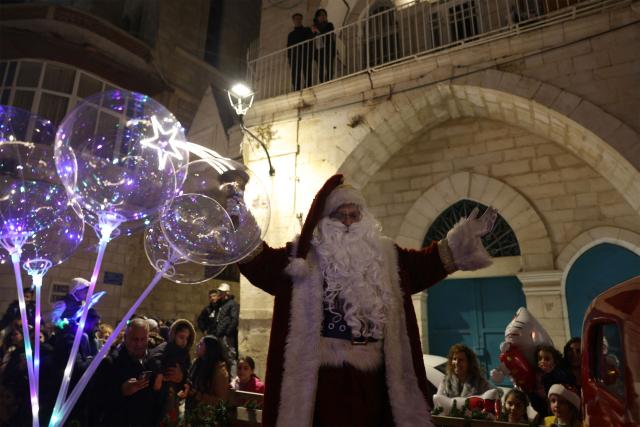 A man dressed as Santa Clause greets pilgrims and Palestinians near Manger Square, in the Israeli-occupied West Bank city of Bethlehem on December 14, 2025. Christmas cheer returned to the traditional birthplace of Jesus Christ on December 6, 2025, the first time the city has held the usual celebrations since the outbreak of the war in Gaza following Hamas's attack on Israel in October 2023. (Photo by HAZEM BADER / AFP)