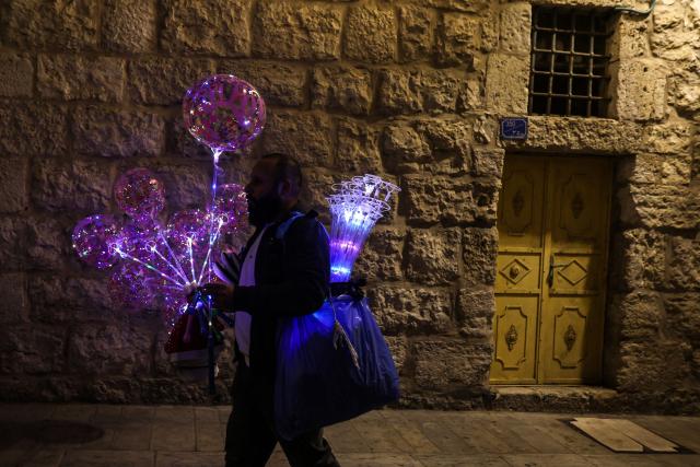 A Palestinian vender sells "light ballons" to pilgrims and Palestinians near Manger Square and the Christmas tree, in the Israeli-occupied West Bank city of Bethlehem on December 14, 2025. Christmas cheer returned to the traditional birthplace of Jesus Christ on December 6, 2025, the first time the city has held the usual celebrations since the outbreak of the war in Gaza following Hamas's attack on Israel in October 2023. (Photo by HAZEM BADER / AFP)
