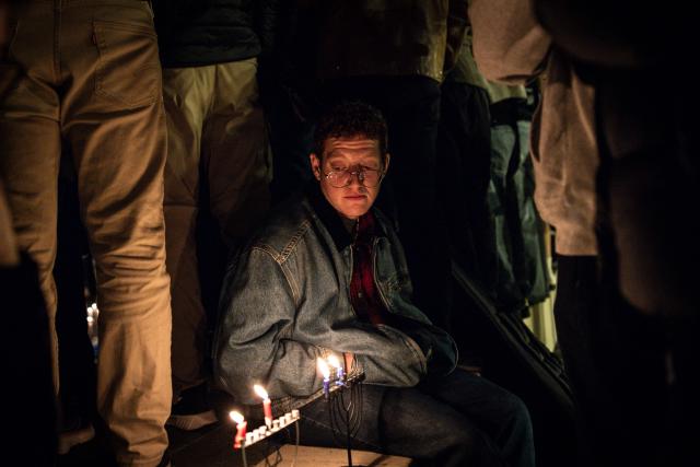 A man sits next to candles during a candlelight vigil hours after two gunmen shot and killed people gathered on Australia's Bondi beach for the Jewish festival of Hanukkah, in Tel Aviv on December 14, 2025. Sixteen people were killed and at least 40 others injured in a shooting at the Jewish festival of Hanukkah celebrations at Australia's Bondi Beach, police said on December 14, 2025 in an update of the casualty toll. (Photo by JOHN WESSELS / AFP)