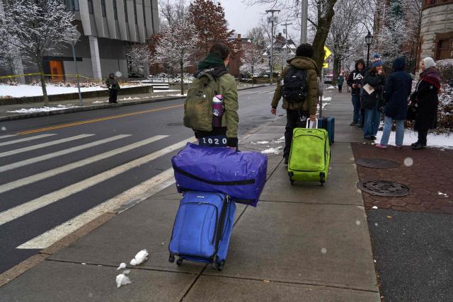 Brown University students carry their luggage as they depart campus after final exams were cancelled the following day of a mass shooting at Brown University, in Providence, Rhode Island on December 14, 2025. US authorities on Sunday detained a person of interest in the mass shooting at Brown University that left two people dead and nine others wounded, the latest in a long line of school attacks nationwide. (Photo by Bing Guan / AFP)