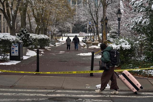 A Brown University student carries her luggage as she departs campus after final exams were cancelled the following day of a mass shooting at Brown University, in Providence, Rhode Island on December 14, 2025. US authorities on Sunday detained a person of interest in the mass shooting at Brown University that left two people dead and nine others wounded, the latest in a long line of school attacks nationwide. (Photo by Bing Guan / AFP)