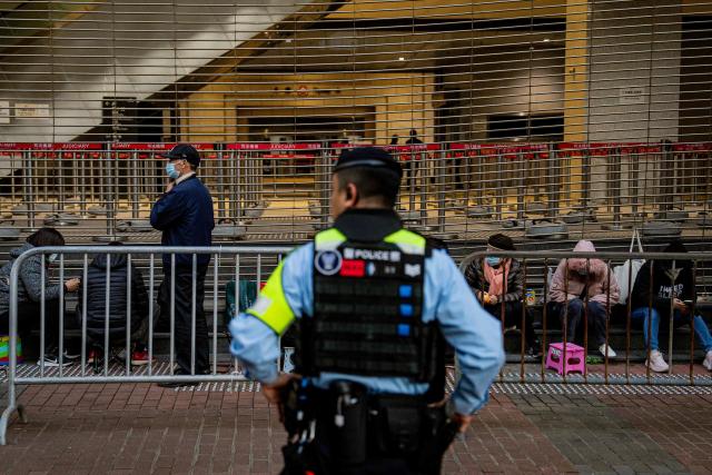 TOPSHOT - A police officer keeps watch as people wait in line to enter the West Kowloon Law Courts building to hear the verdicts in the national security trial of pro-democracy media tycoon Jimmy Lai in Hong Kong on December 15, 2025. Long-awaited verdicts in Hong Kong pro-democracy media tycoon Jimmy Lai's national security trial will be delivered on December 15, one of the city's most closely watched rulings since its return to Chinese rule in 1997. (Photo by Leung Man Hei / AFP)