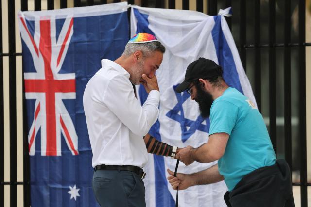 Co-CEO of the executive council of Australia Jewry Alex Ryvchin (L) prays with a rabbi as they stand outside the Bondi Pavilion, where an Australia and Israeli flag are displayed in memory of the victims of a shooting at Bondi Beach, in Sydney on December 15, 2025. A father-and-son team toting long-barrelled guns shot and killed 15 people including a 10-year-old girl at Sydney's Bondi Beach, authorities said on December 15, labelling it an antisemitic terrorist attack on a Jewish festival. (Photo by DAVID GRAY / AFP)