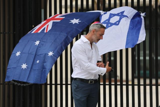 Co-CEO of the executive council of Australia Jewry Alex Ryvchin stands outside the Bondi Pavilion, where an Australia and Israeli flag are displayed in memory of the victims of a shooting at Bondi Beach, in Sydney on December 15, 2025. A father-and-son team toting long-barrelled guns shot and killed 15 people including a 10-year-old girl at Sydney's Bondi Beach, authorities said on December 15, labelling it an antisemitic terrorist attack on a Jewish festival. (Photo by DAVID GRAY / AFP)