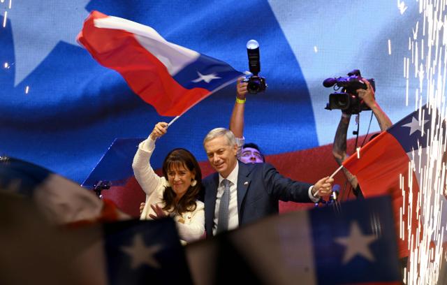 Chile's presidential candidate Jose Antonio Kast (R), of the Partido Republicano party, and his wife Maria Pia Adriasola (L) wave national flags as they celebrate the results of the presidential runoff election in Santiago on December 14, 2025. Chilean voters elected Jose Antonio Kast, the most right-wing president in 35 years of democracy, with a thumping 58 percent of votes and his rival Jeannette Jara conceding defeat, according to official results on December 14, 2025. (Photo by Eitan ABRAMOVICH / AFP)