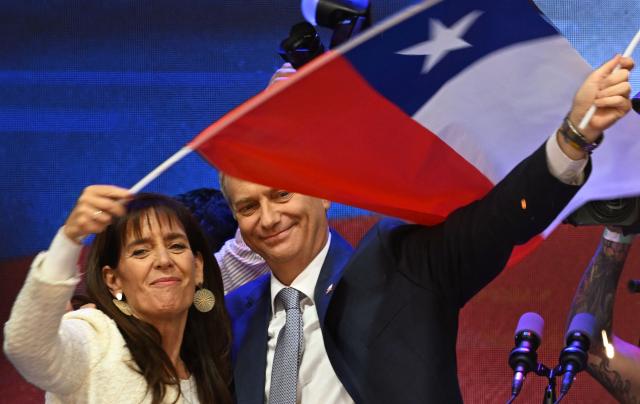 Chile's presidential candidate Jose Antonio Kast (R), of the Partido Republicano party, and his wife Maria Pia Adriasola (L) wave national flags as they celebrate the results of the presidential runoff election in Santiago on December 14, 2025. Chilean voters elected Jose Antonio Kast, the most right-wing president in 35 years of democracy, with a thumping 58 percent of votes and his rival Jeannette Jara conceding defeat, according to official results on December 14, 2025. (Photo by Eitan ABRAMOVICH / AFP)