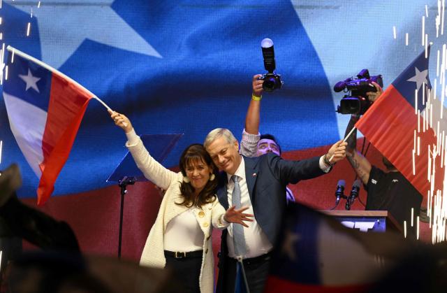 Chile's presidential candidate Jose Antonio Kast (R), of the Partido Republicano party, and his wife Maria Pia Adriasola (L) wave national flags as they celebrate the results of the presidential runoff election in Santiago on December 14, 2025. Chilean voters elected Jose Antonio Kast, the most right-wing president in 35 years of democracy, with a thumping 58 percent of votes and his rival Jeannette Jara conceding defeat, according to official results on December 14, 2025. (Photo by Eitan ABRAMOVICH / AFP)